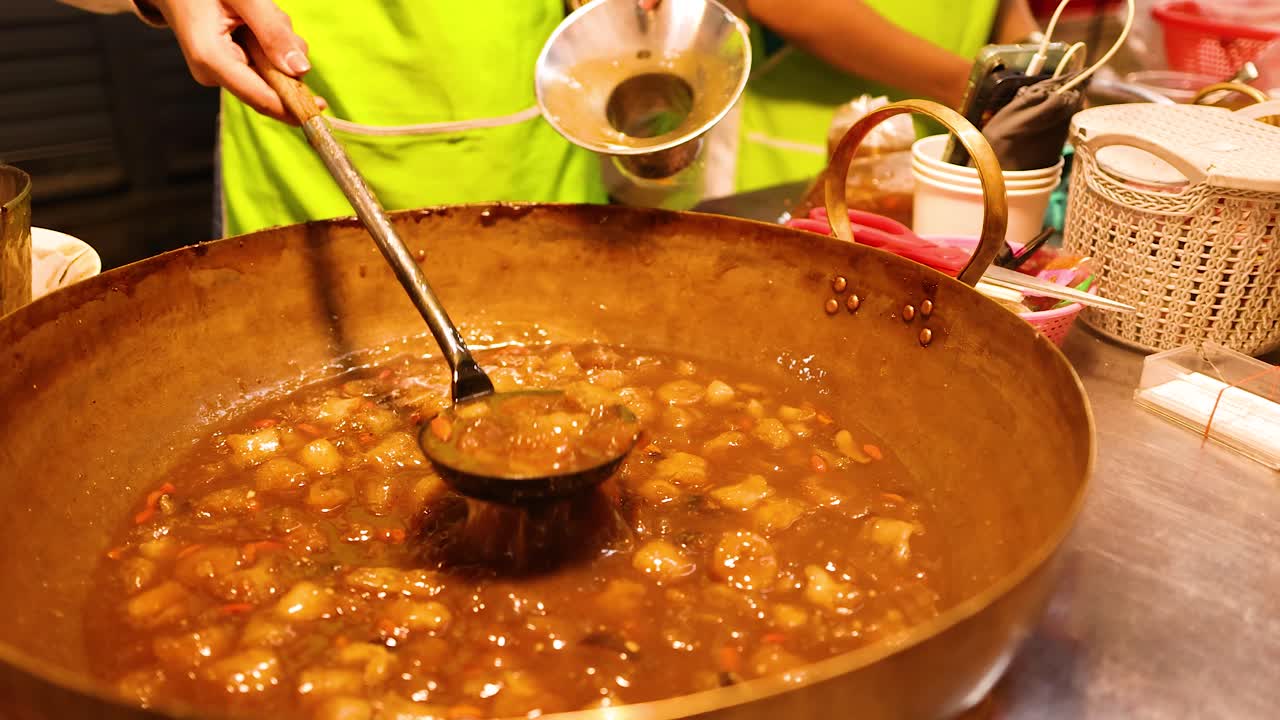 Vendor ladles hot fish maw soup from large pot under warm lights, close-up street food