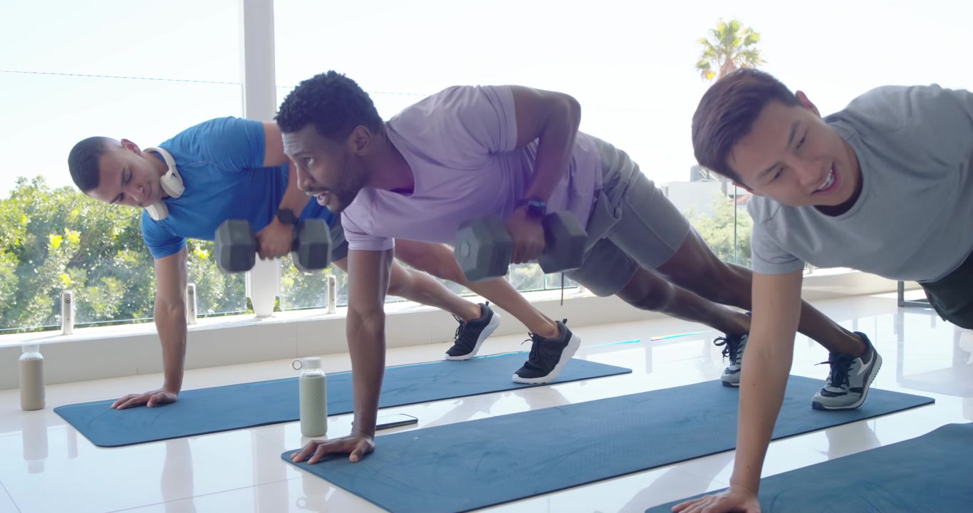 Trois hommes commençant des tractions en planche sur des tapis bleus près d'un mur en verre, utilisant des haltères hexagonaux, pour le gainage.