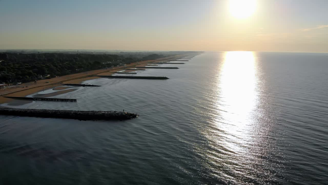 Ripresa aerea orizzontale sull'acqua, con moli sulla sinistra lungo la costa e una spiaggia sabbiosa, realizzata con drone.