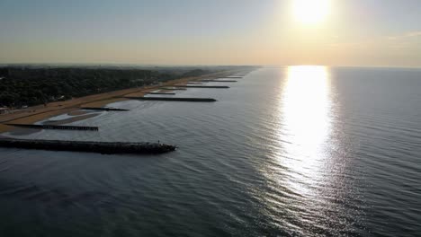 aerial horizontal shot over water, passing bye piers on the left along the coastline, sandy beach, drone shot