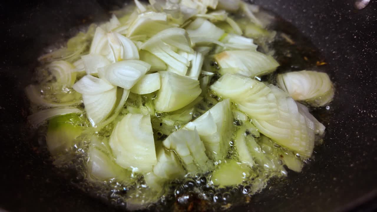 Primo piano di cipolle a cubetti che sfrigolano in olio bollente in una padella per la preparazione di cibo e progetti culinari in cucina