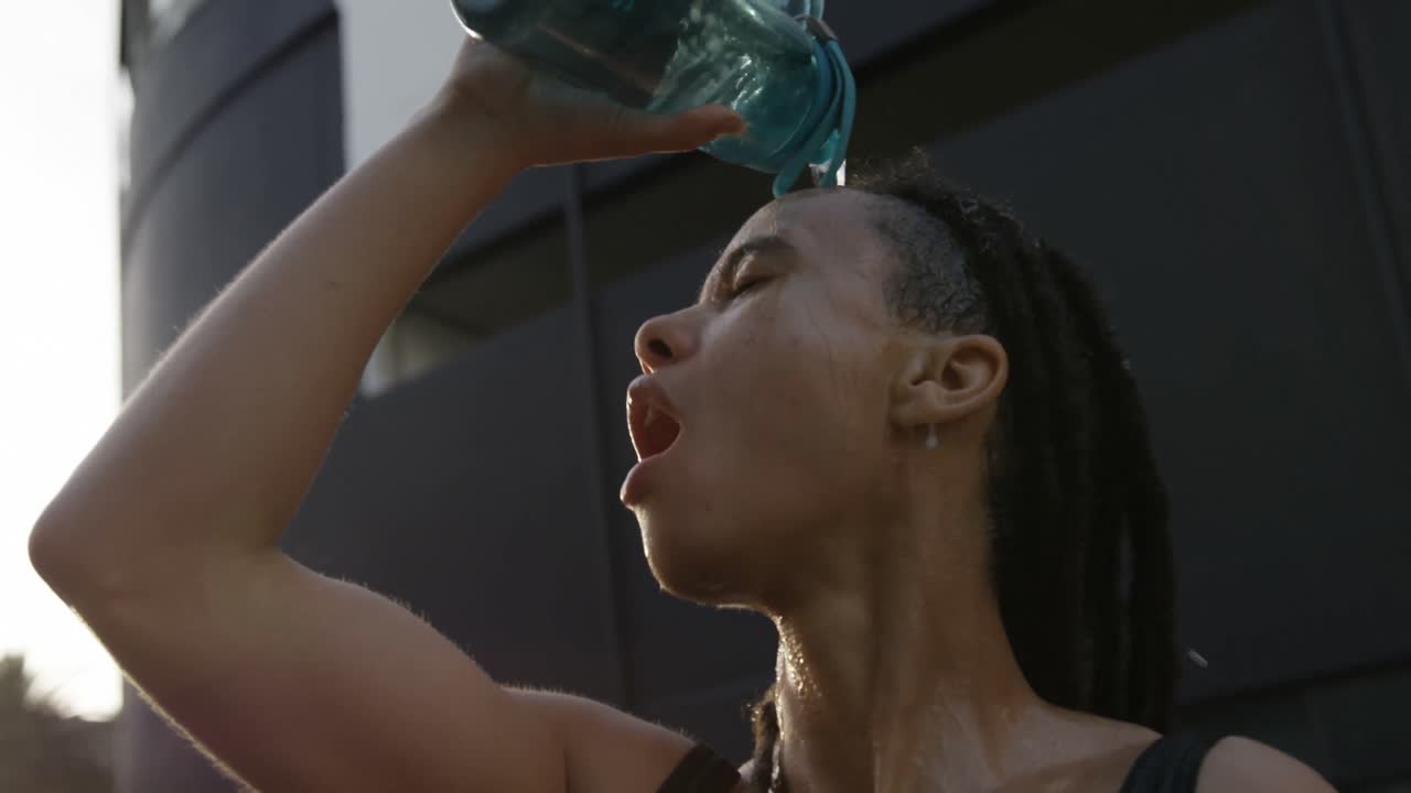 vista frontal de una joven mujer afroamericana vertiendo agua en su cabeza en la ciudad 4k