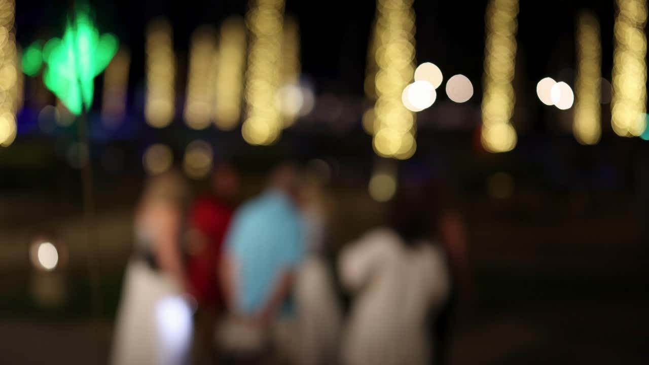 A group of people socializing at a resort during nighttime, captured with intentional blur and vibrant lighting