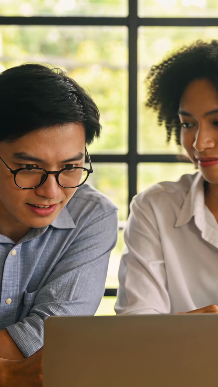 Vertical video: Spotting result on laptop, coworkers in shirts leaning in at table, reviewing work