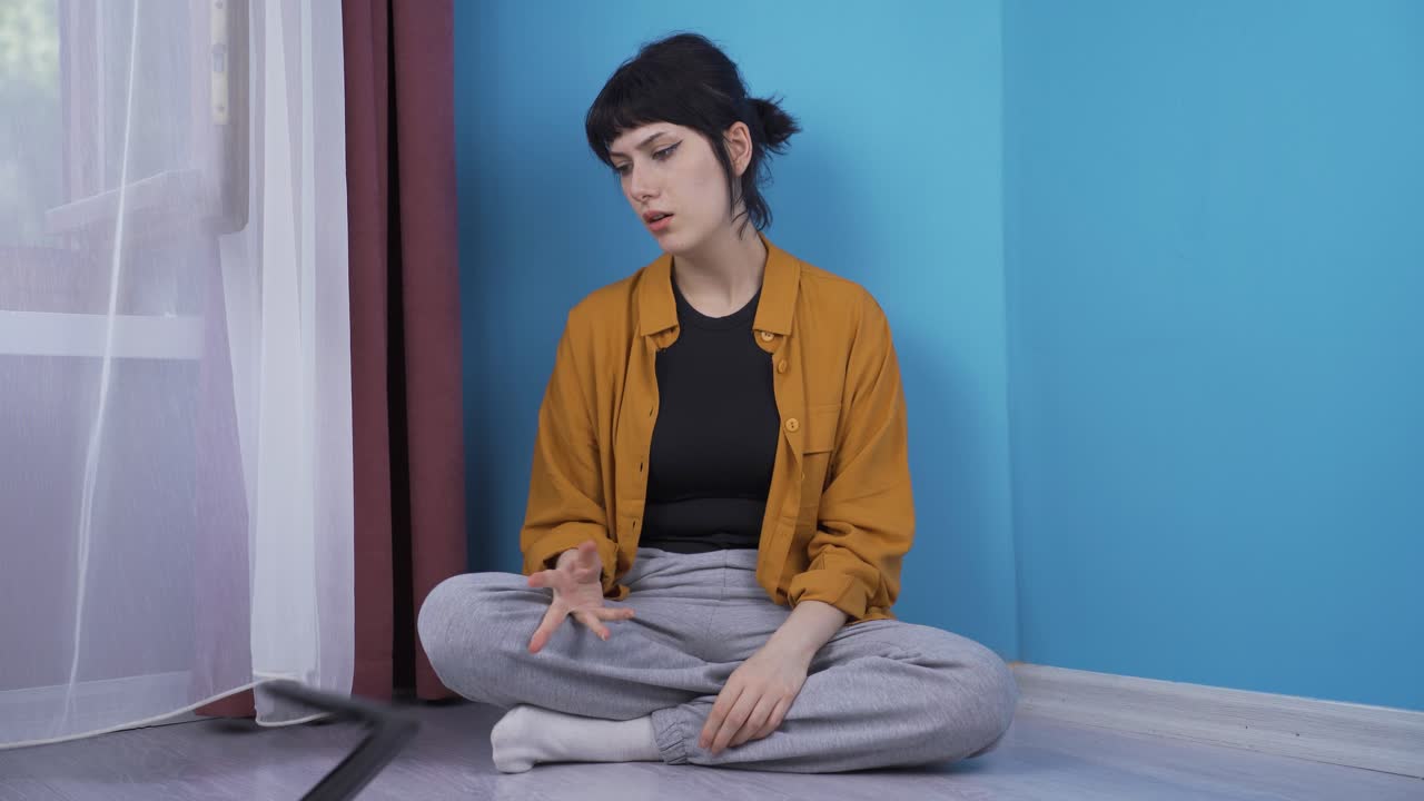 la joven sentada junto a la pared mira su billetera vacía.