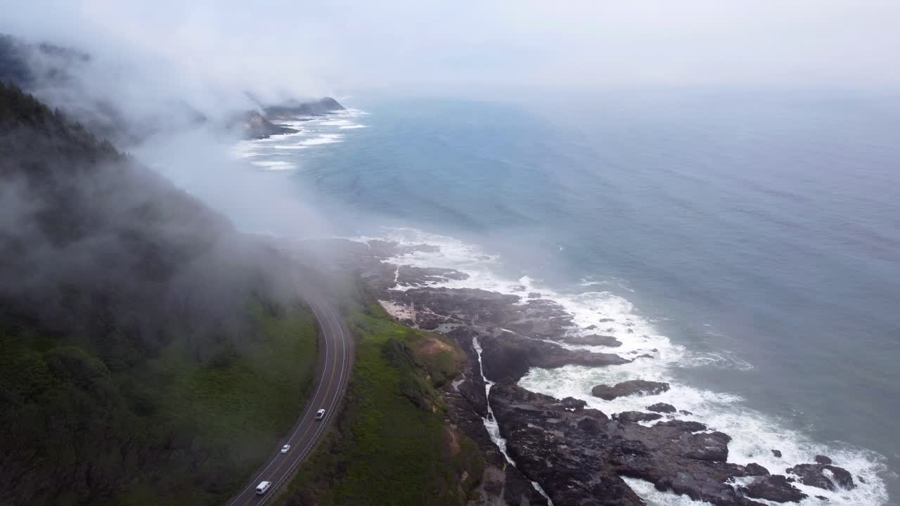 imágenes aéreas de 4.000 fps de la costa de oregón - toma estática épica de la ruta 101 y el tráfico de automóviles - volando entre nubes, olas chocando contra rocas de piedra cubiertas de musgo en la costa del océano pacífico - video de drones dji