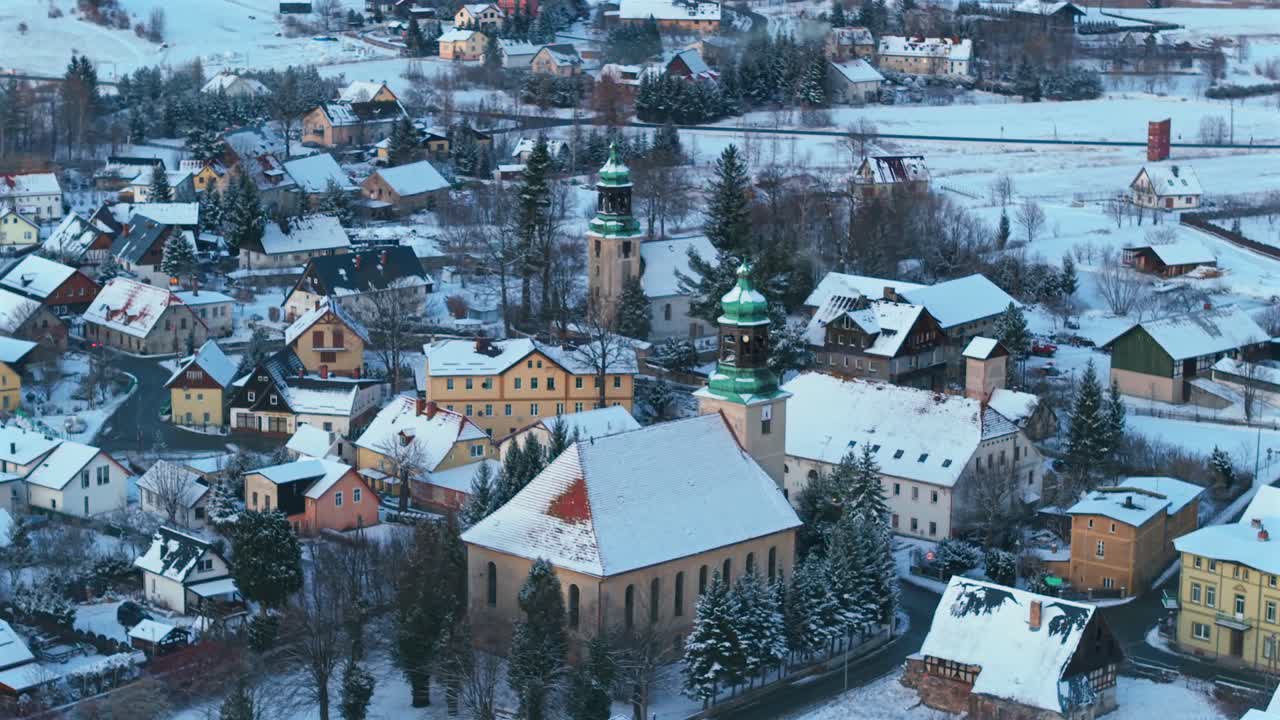 Široký letecký pohled, vesnická krajina při západu slunce, kostely, zasněžené počasí.