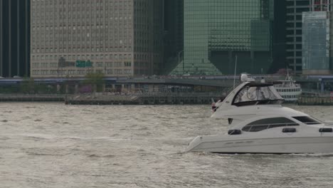 a small yacht and jet ski make their way up new york bay as traffic traverses the fdr drive in manhattan in the backdrop