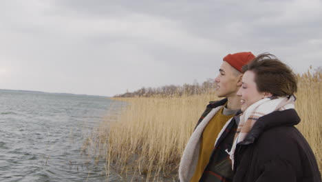 side view of a teenage boy and teenage girl talking standing near of seashore on a cloudy day