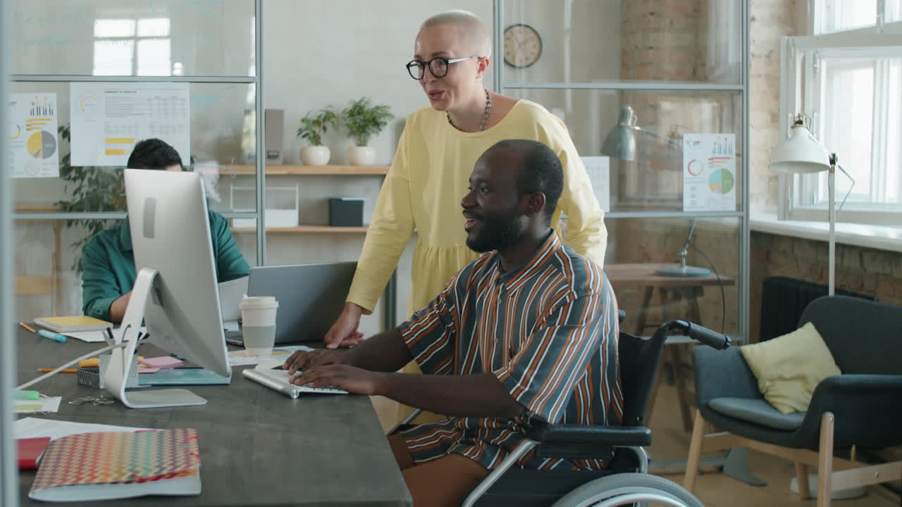 Black Businessman in Wheelchair Working with Female Colleague in Office