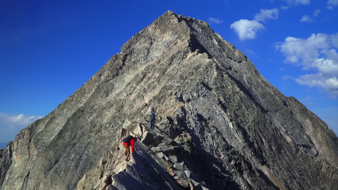 Knifes Edge Capitol Peak north east ridge Wilderness Trail Hikers scrambling rock climbing Rocky Mountains Colorado 14er mountainside large boudlers aerial view summer blue sky morning sunny clouds