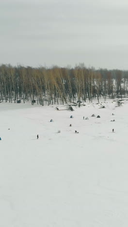 fishermen silhouettes settle on ice of frozen river surface covered with snow near thick pine tree forest aerial view