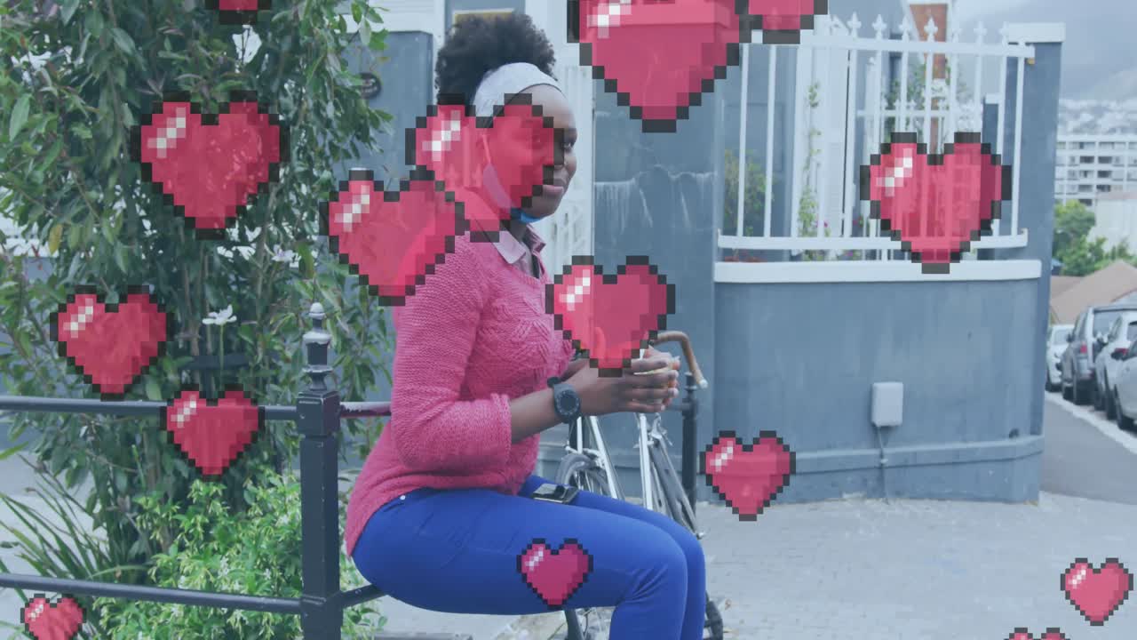 Animatie van pixelhartjes over een blije Afro-Amerikaanse vrouw met mondkapje die eet op straat