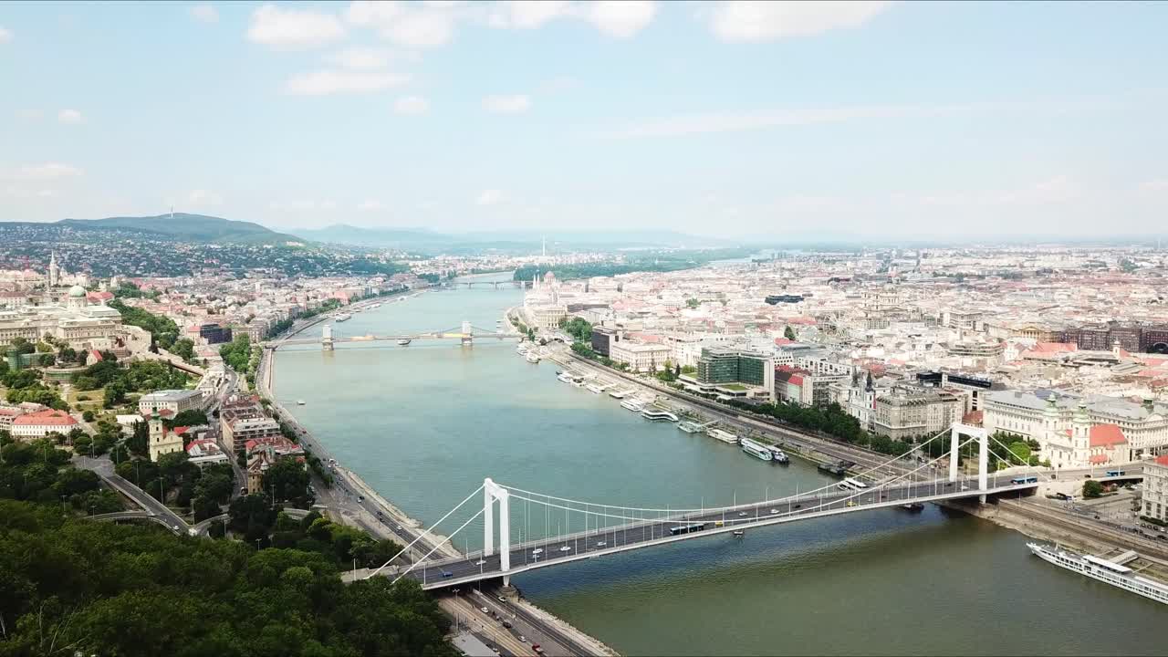 Aerial view of Budapest, Hungary, featuring the Liberty Statue atop Gellért Hill, overlooking the Danube River, the Elizabeth Bridge, and historic cityscape with iconic landmarks and vibrant scenery