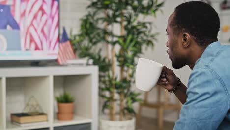 Tracking-video-of-black-man-drinking-coffee-and-watching-TV