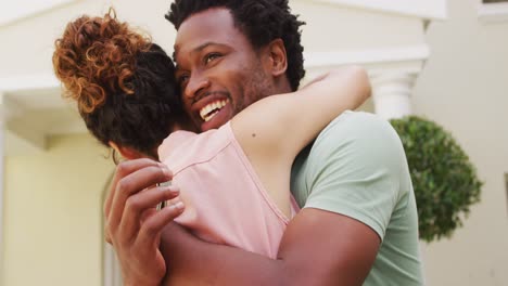 feliz pareja biracial abrazándose con alegría frente a la nueva casa