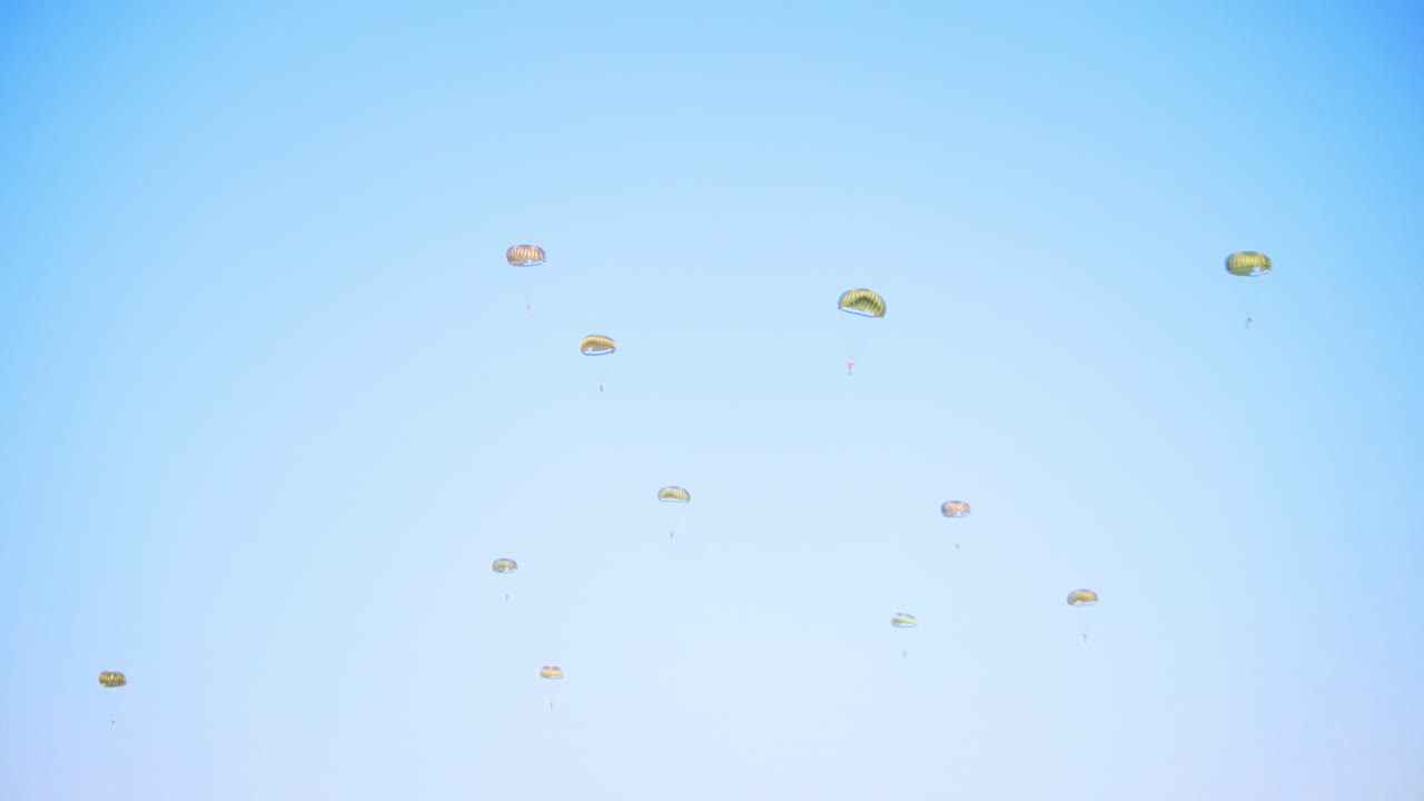 여러 개의 낙하산이 은 파란 하늘을 배경으로 조정된 군사 훈련 연습에서 하늘에서 부드럽게 내려옵니다.