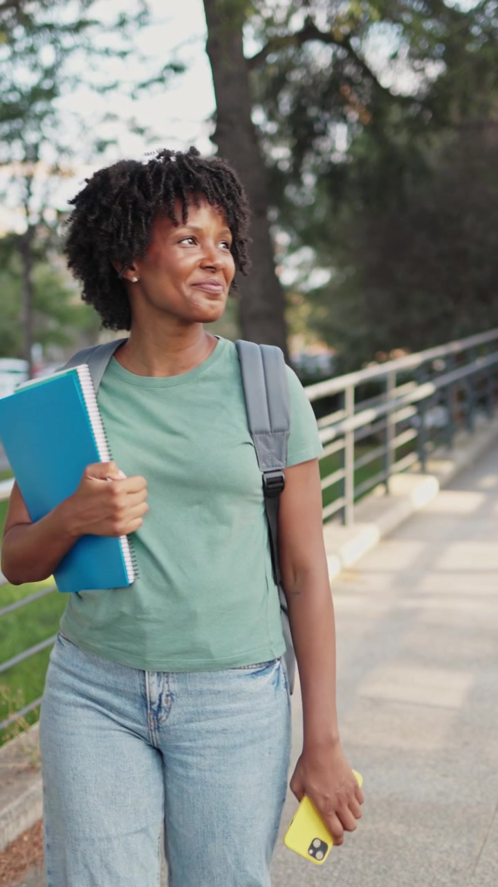 Felice studentessa afroamericana che cammina all'aperto mentre usa il telefono