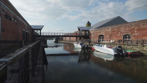 Leere-Kleine-Hakodate-Kreuzfahrtboote,-Die-Im-Yachthafen-Angedockt-Sind,-Mit-Blick-Auf-Den-Brückensteg,-Der-Mit-Dem-Lagerhaus-Aus-Rotem-Backstein-Von-Kanemori-Verbunden-Ist