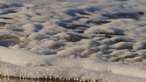 white foamy water on beach with storm surge barrier in background at oosterschelde, super slow motion