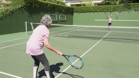 Kaukasisches-älteres-Paar,-Das-Auf-Einem-Außenplatz-In-Der-Sonne-Eine-Partie-Tennis-Spielt