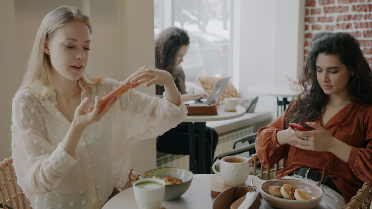 Young Women Enjoying Breakfast and Social Media in a Cafe