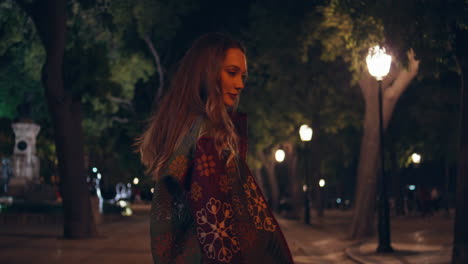 chica alegre caminando en el parque de la ciudad oscura a las luces de la calle de cerca. modelo posando callejón