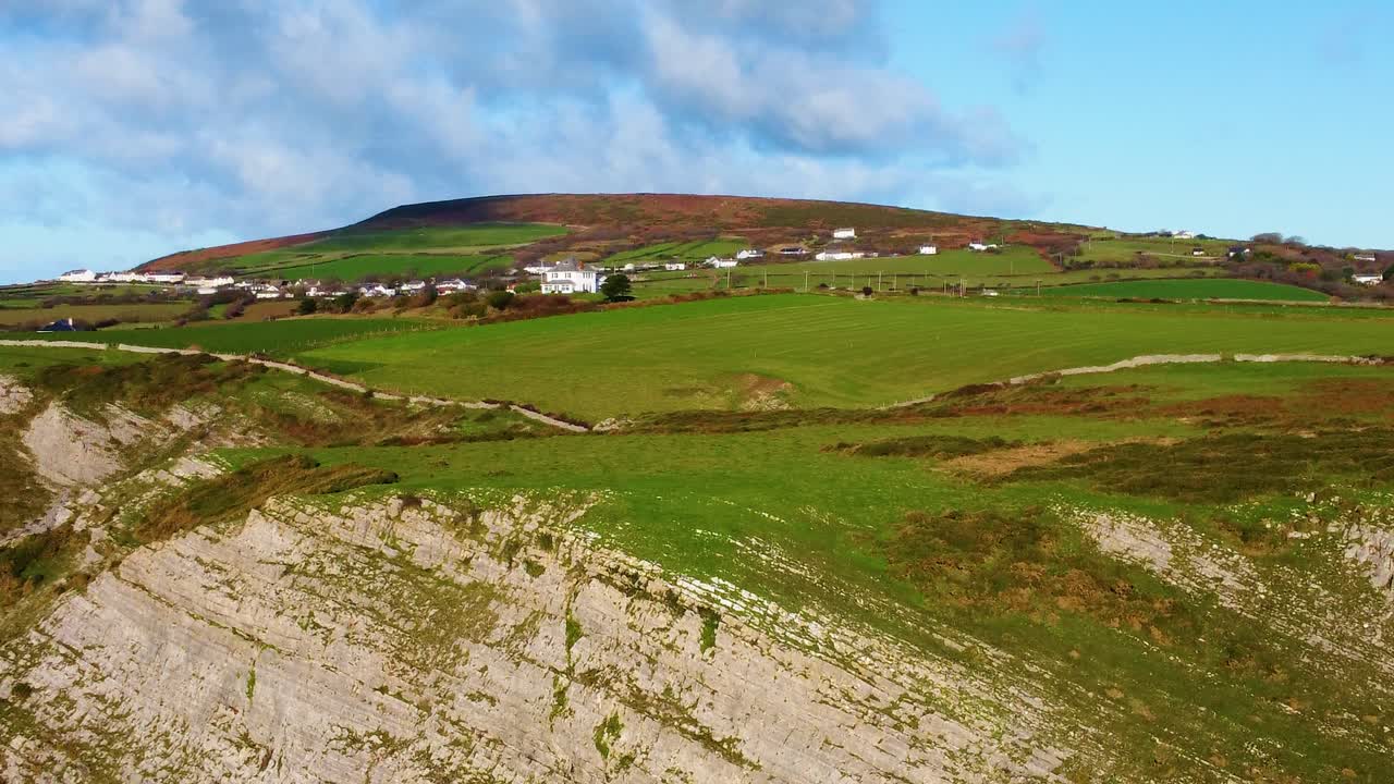 Orbiting Aerial View of Gower Coastline with Lone House on Hill with Rhossili Village in Background. Steep Coastal Cliffs and Stone Wall Lining Coast Path. Nature Drone Clip