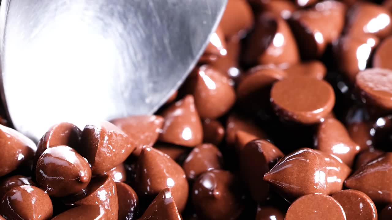 A spoon delicately scoops glossy chocolate chips, highlighting their shiny texture and rich brown color.