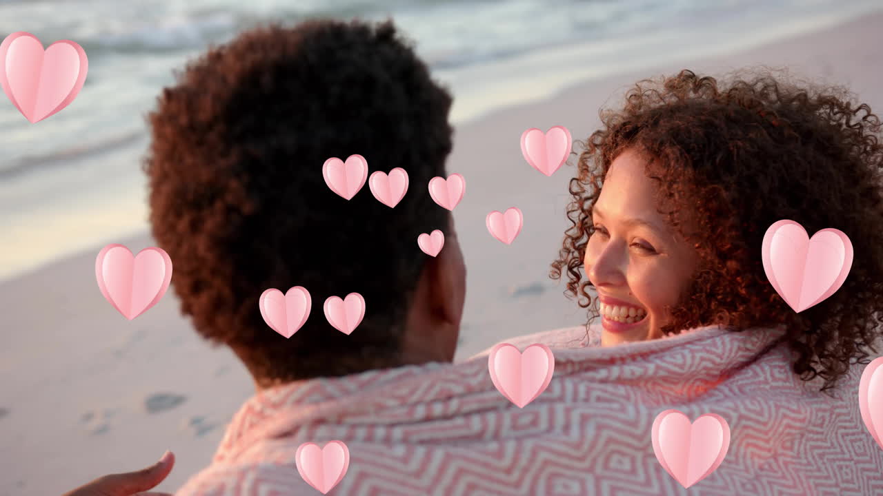 Animation of hearts moving over diverse couple in love embracing on beach in summer