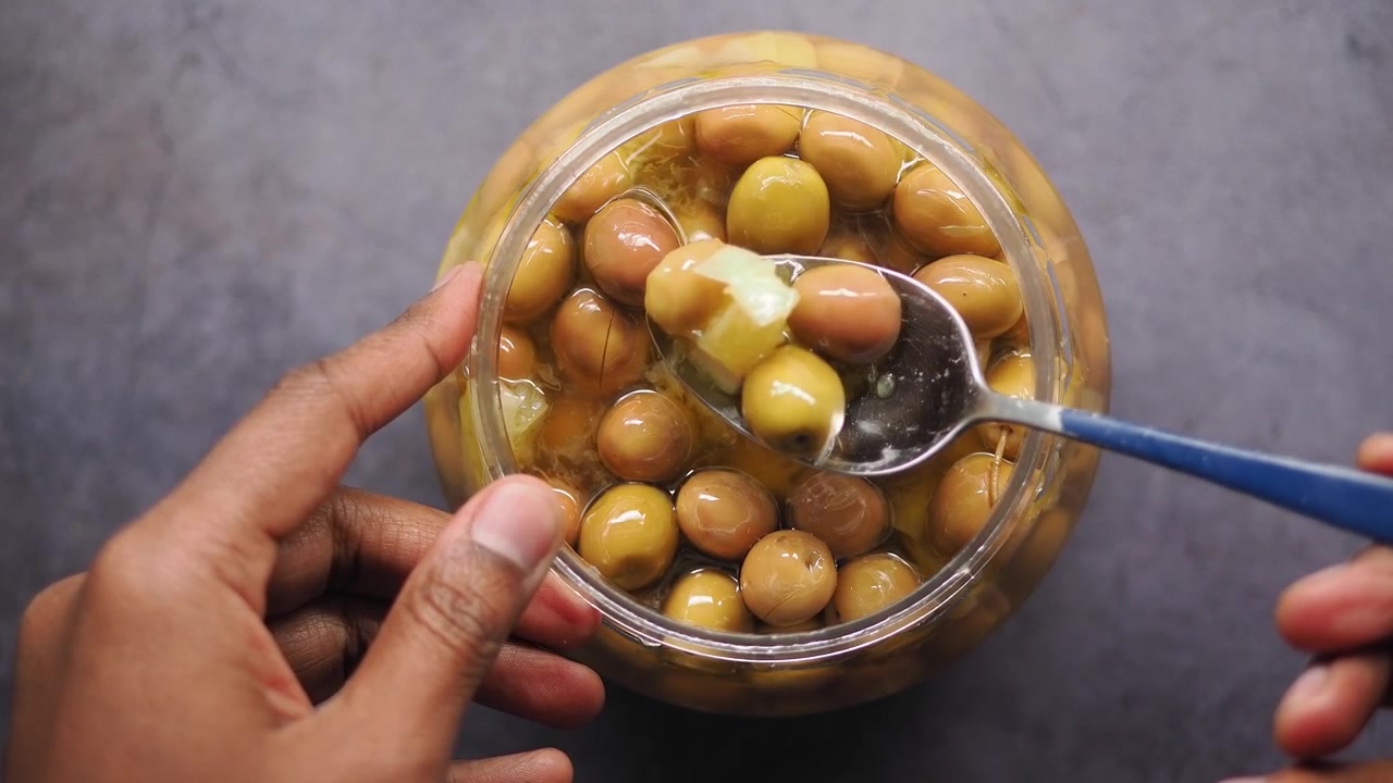 Mano che preleva olive verdi sottaceto da un barattolo