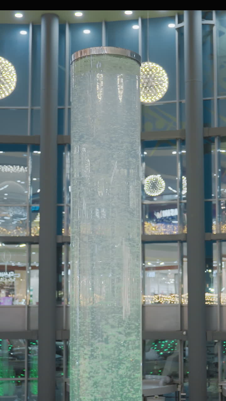 Beautiful view of Christmas decorations in a mall with glowing Christmas lights, festive ornaments, and a large cylindrical water feature in the center, creating a cozy holiday atmosphere