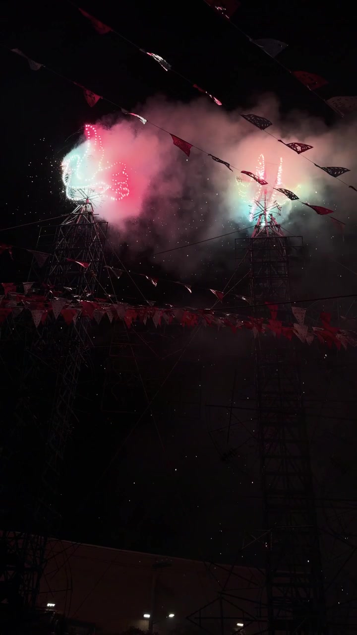 Pyrotechnic castle spins and ignites with fireworks during traditional religious festival at night, vertical