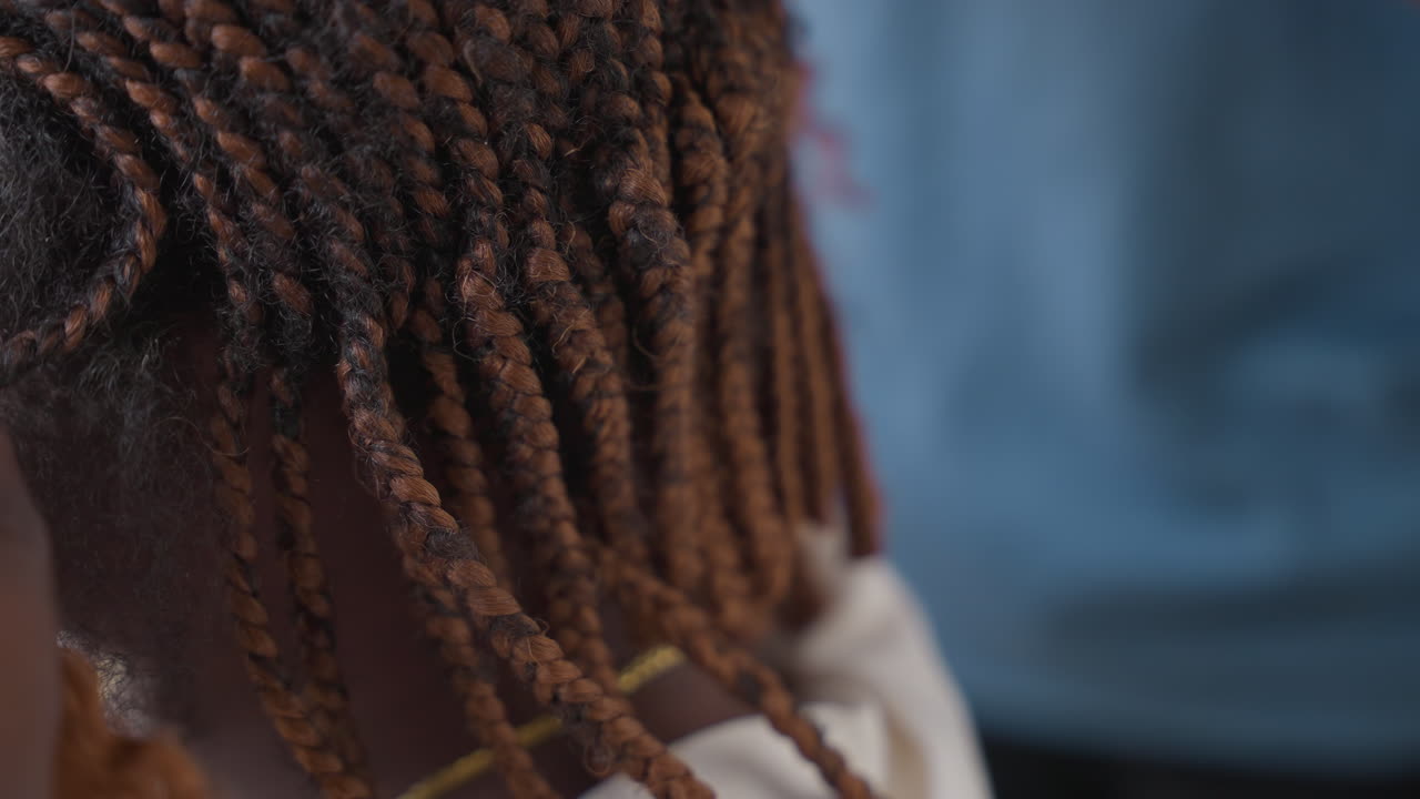 Primo piano di ispezione dei capelli intrecciati di un bambino. Stilista esperto e assistente esaminano le file di microtrecce, regolano la tensione con dita attente, controllano le radici per detriti, mostrano il motivo e la texture con delicatezza.