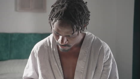 Guy in bathrobe sitting on bed, deeply engrossed in reading a book. Soft light from window enhances peaceful, relaxed indoor atmosphere. Comfortable setting with cozy bedding and tranquil mood