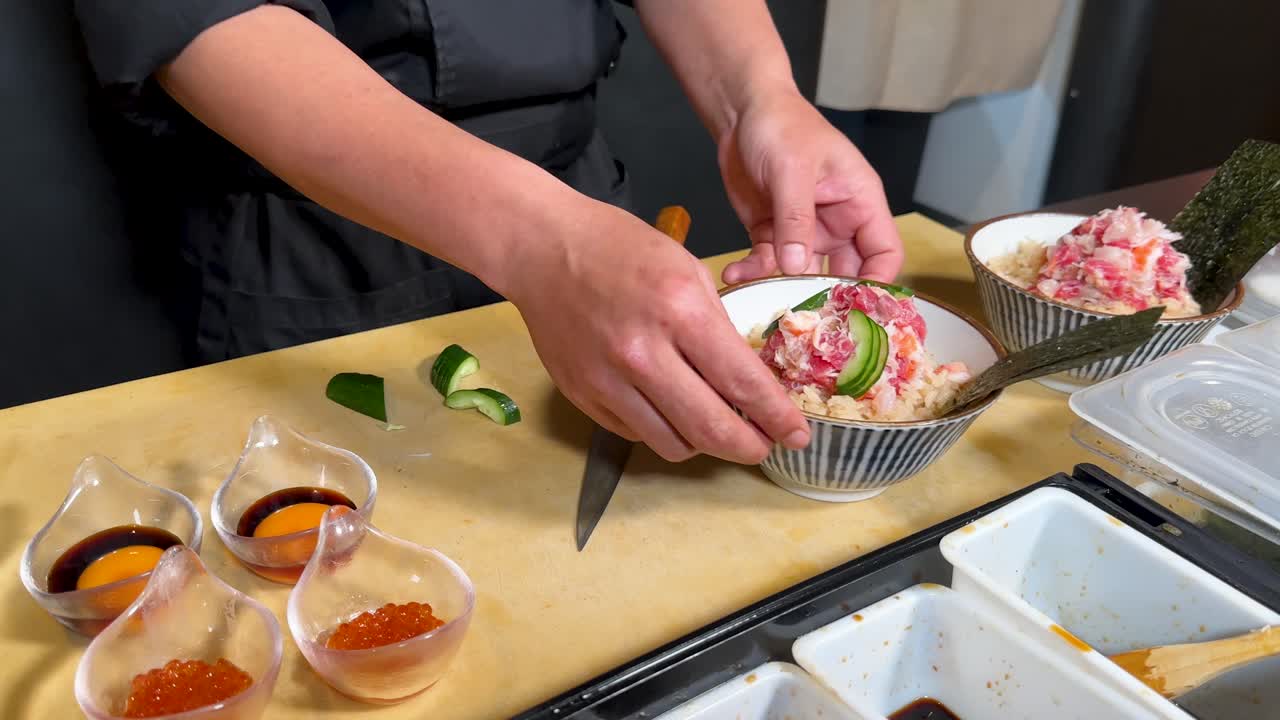 黒いコートを着たプロのシェフが、丁寧にキュウリで刺身丼を飾り付けています。