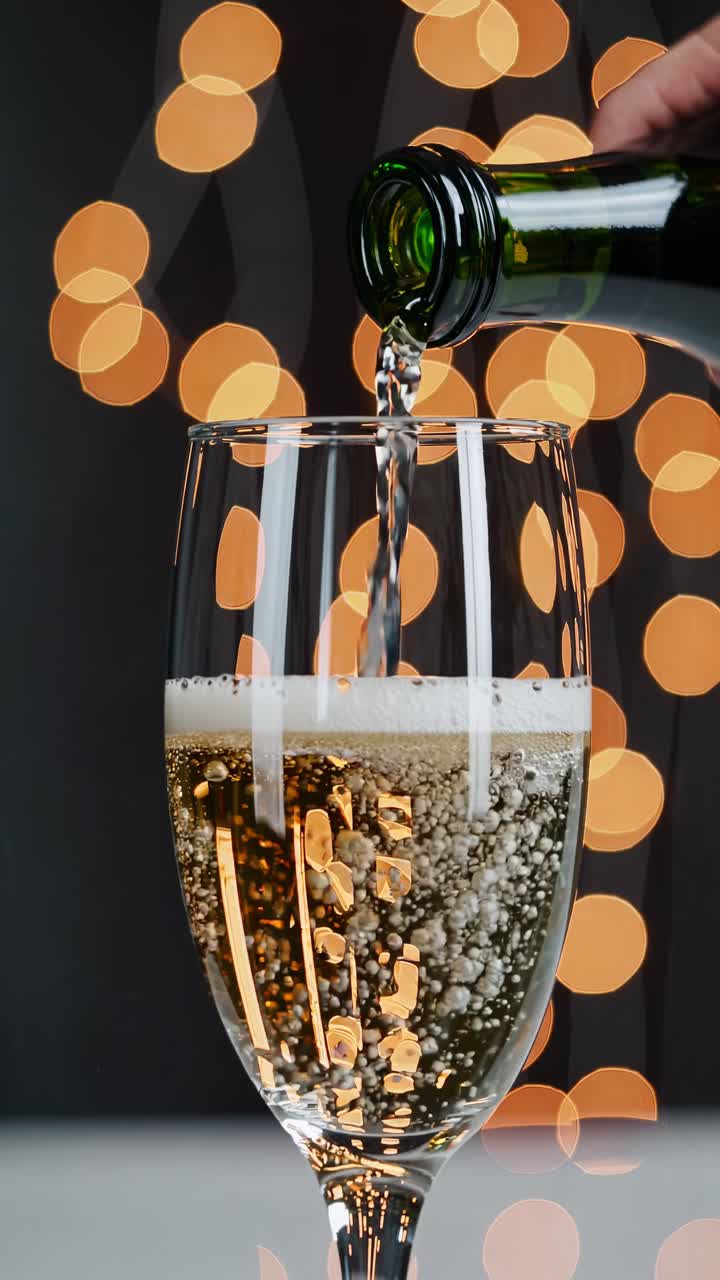 Close-up video of champagne being poured into a glass, with a bokeh background of warm lights