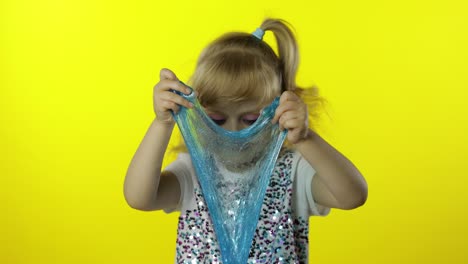 kid playing with hand made toy slime. child having fun making turquoise slime. yellow background