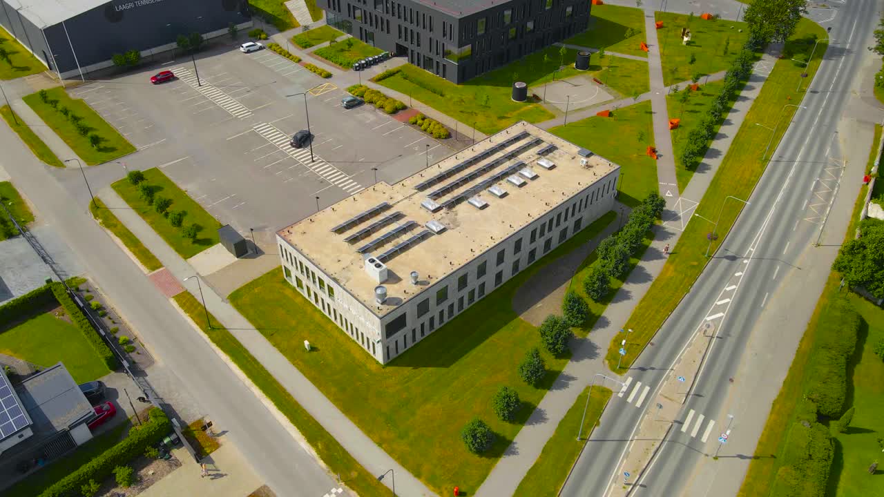 Aerial drone footage orbiting around a modern gray colored concrete building that is a health and medical centre in Saue laagri Estonia during a sunny summer day with roads and green parks around it