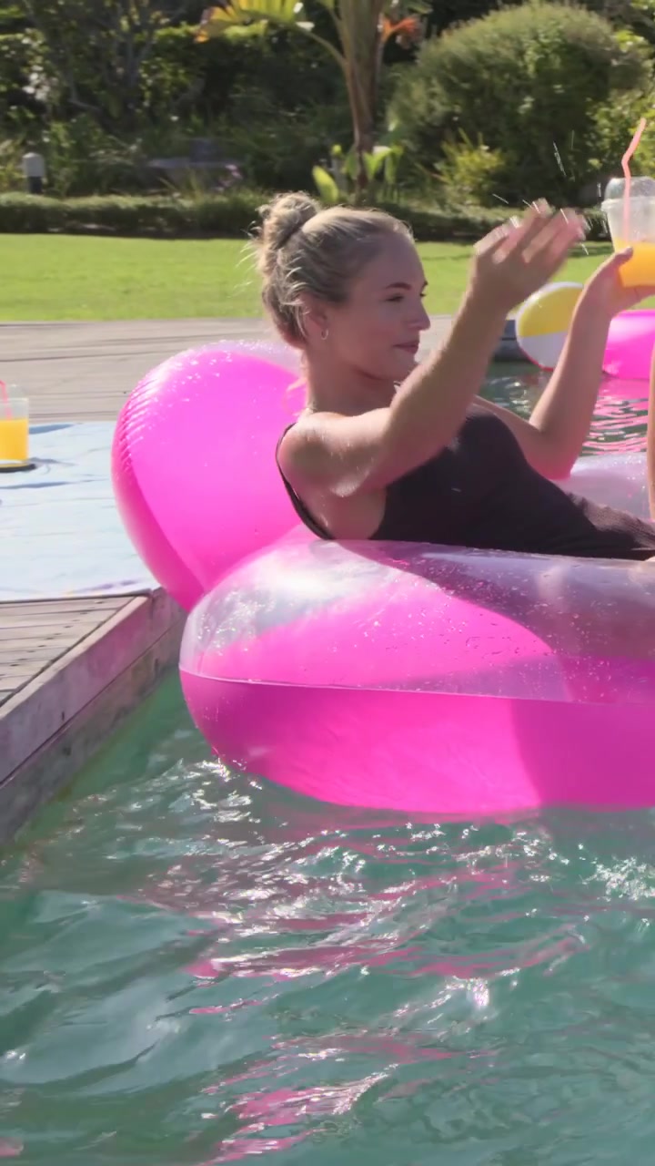 Vertical video: Drifting float nudging woman dark swimsuit reaching pool deck for cup, copy space