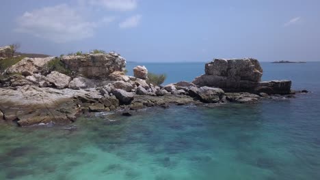 antena: plataforma rodante a baja altura en una toma a través de una amplia abertura en una formación rocosa parcialmente sumergida en el agua, y que revela una hermosa isla tropical en la distancia