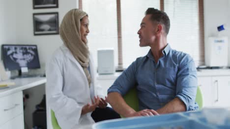 Biracial-female-dentist-talking-with-male-patient-at-modern-dental-clinic