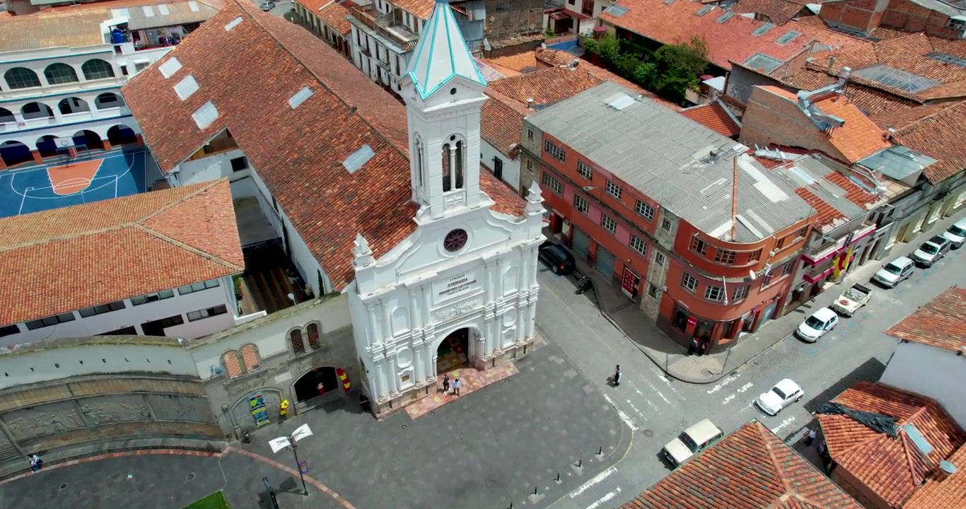 Drone cinematografico che vola in avanti avvicinandosi alla bellissima chiesa di La Merced a Cuenca, Ecuador, rivelando lo splendido skyline storico della città sullo sfondo in una splendida giornata limpida e soleggiata con cieli azzurri.