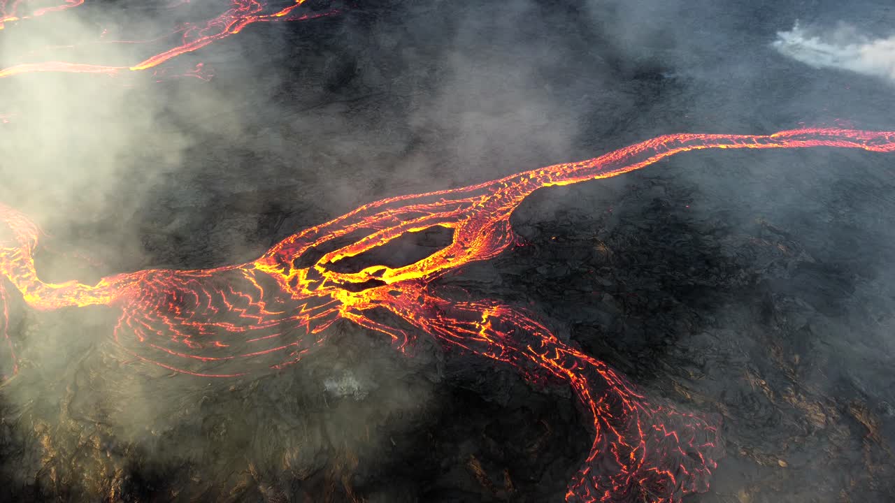 Lava flowing at the eruption site in Iceland, while smoke billows from the crater
