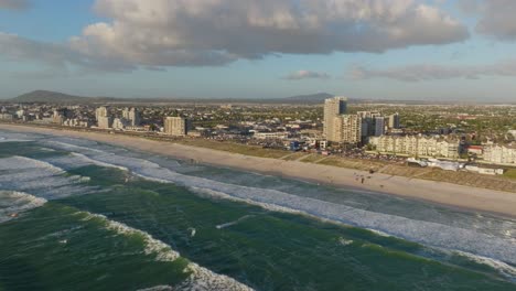 ocean waves roll toward blouberg's shore with urban village in the backdrop