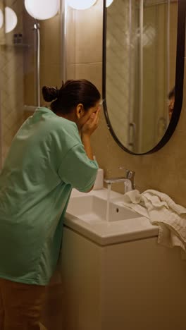 Confident-brunette-girl-with-Brown-skin-color-in-green-pajamas-is-working-at-the-sink-and-washing-her-hands-while-getting-ready-for-bed-in-the-evening-in-the-bathroom