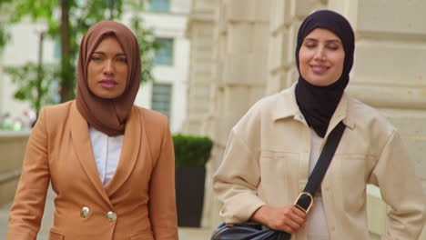 two muslim businesswomen wearing hijabs with modern business suits walking to work past city office buildings 3