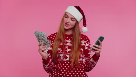 girl in red christmas sweater using mobile phone, hold money dollar cash, doing online gift shopping