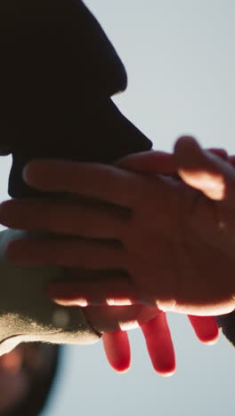 close-up of three individuals stacking their hands together in a gesture of unity and teamwork against a clear sky background