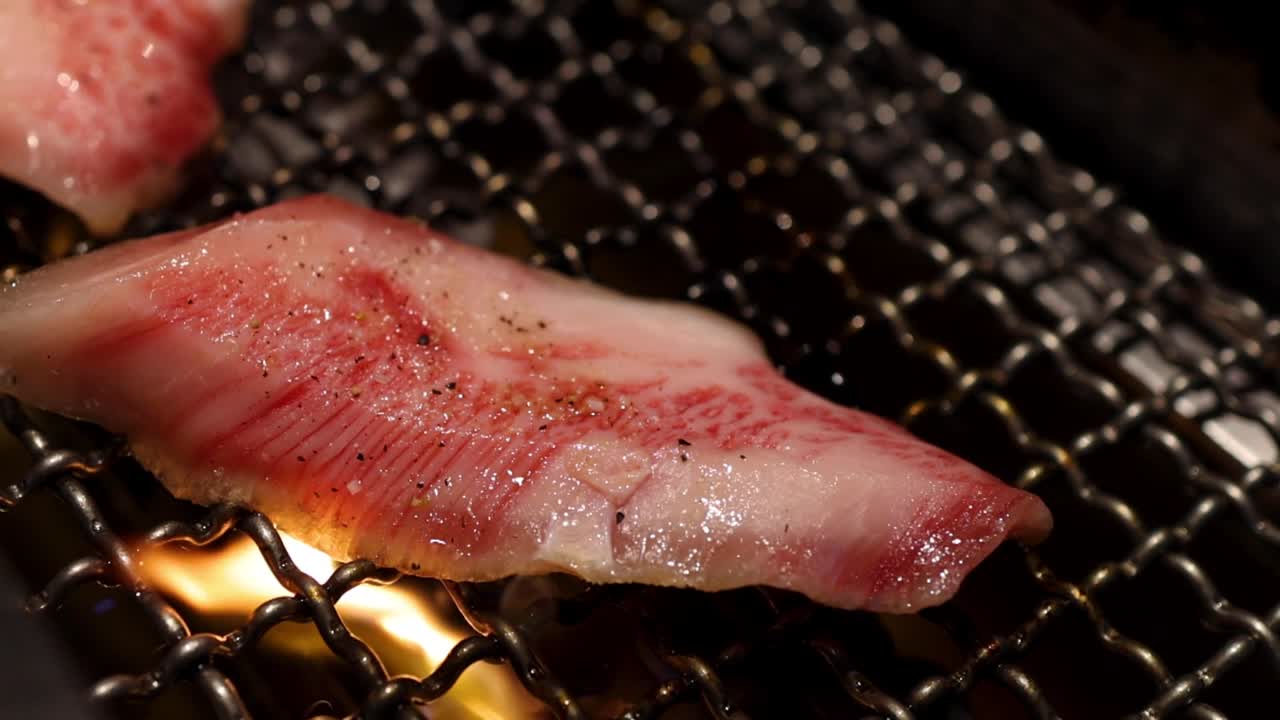 Close-up of marbled meat sizzling over a hot charcoal grill with occasional flames.
